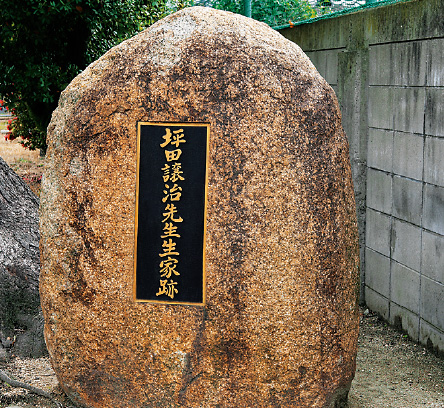 「坪田譲治先生生家跡」と刻まれた銅版がはめ込まれた万成石の「石碑」の写真